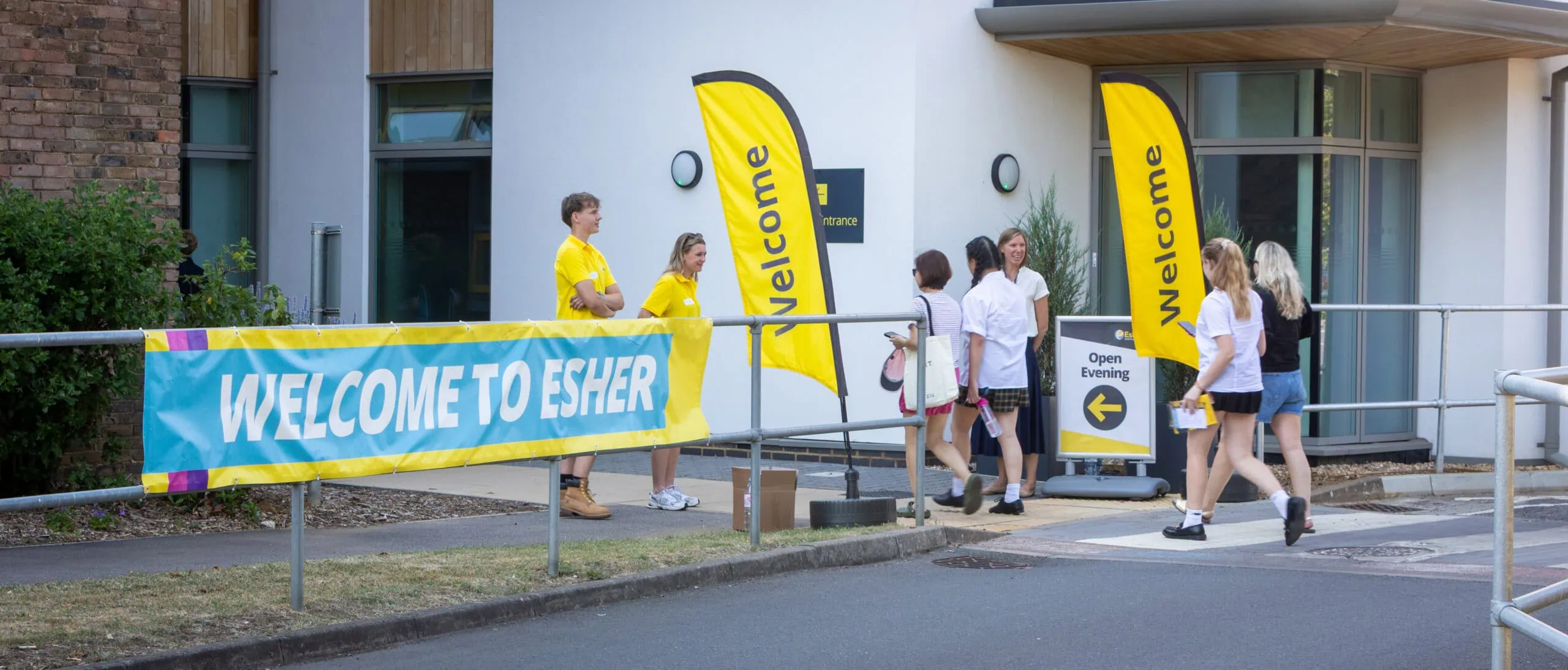 students and staff stand outside the college student entrance to welcome visitors 